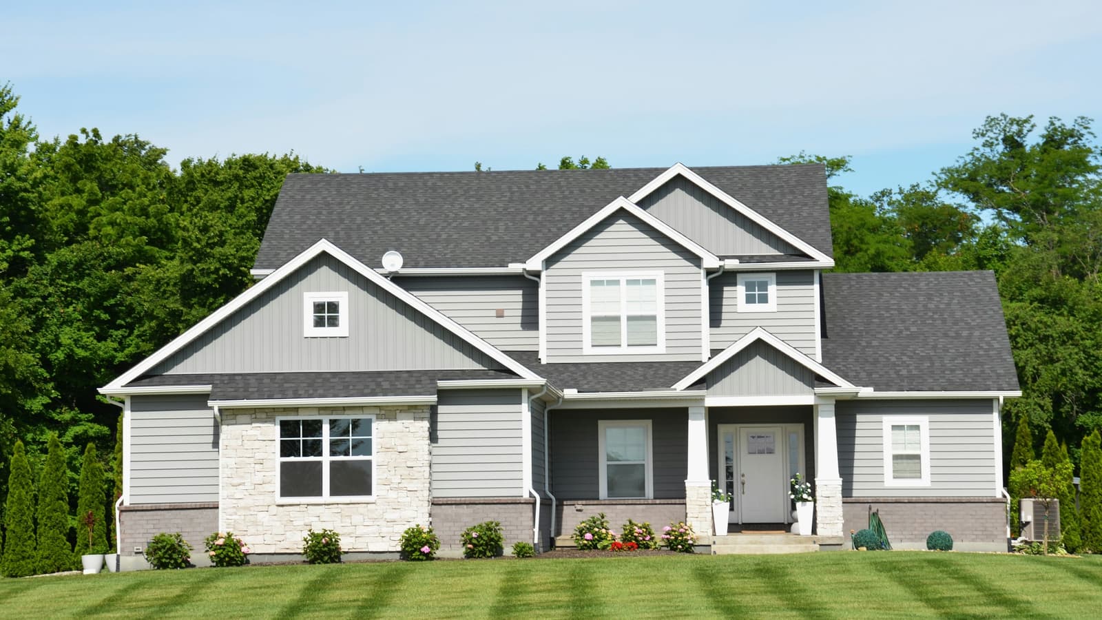 Gray two-story suburban house with stone accents and manicured striped lawn